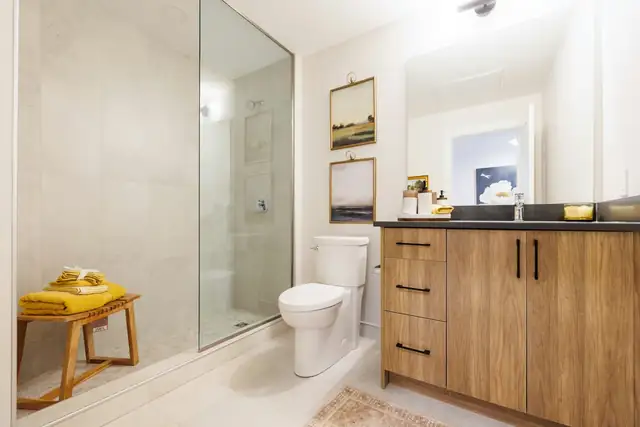 Remodeled bathroom with frameless glass walk-in shower, large light stone tile and a warm wood vanity with black pulls