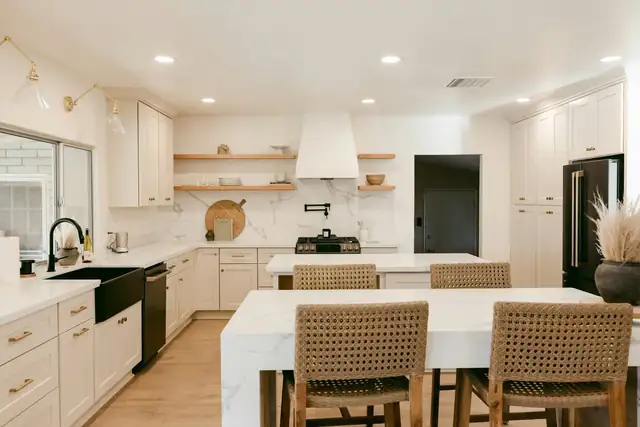 White kitchen remodel with waterfall quartz island, woven counter stools, open oak shelves and a plaster range hood