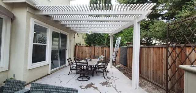 White lattice patio cover over a concrete side yard patio with outdoor dining set