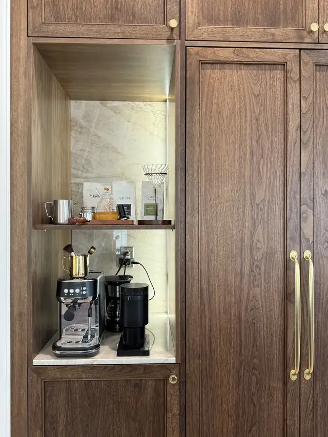 Built-in walnut coffee bar cabinet with a lit stone back panel and long brass handles